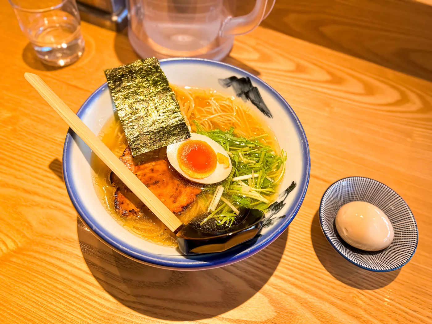 A bowl of ramen with sliced pork, egg, nori and greens