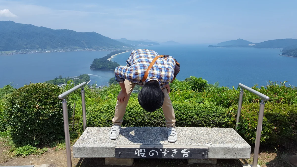 A visitor bending forward on a designated platform to look at Amanohashidate between their legs
