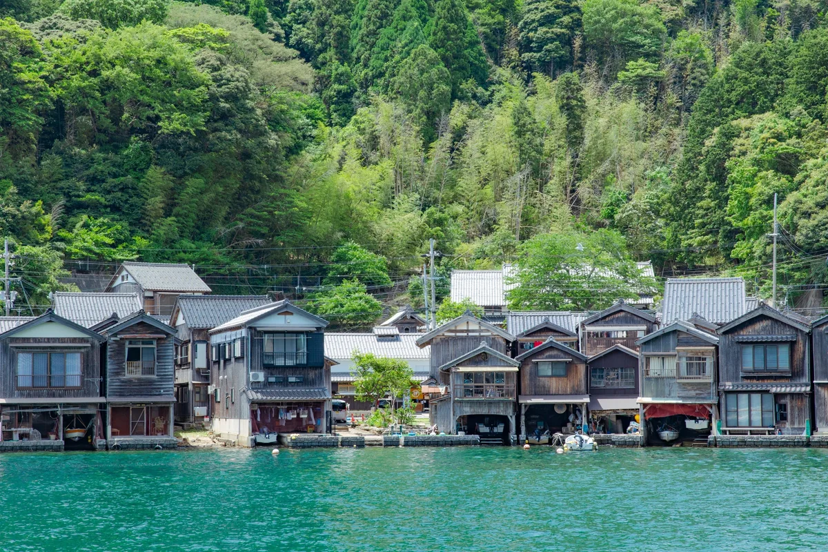Ine's wooden boathouses beside turquoise water with green woodland rising behind them