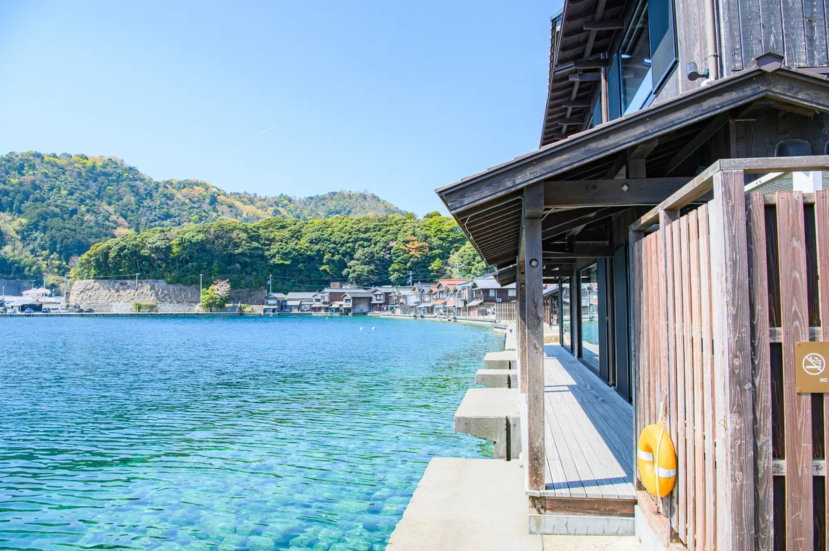 A wooden building and railing immediately beside clear blue water in Ine