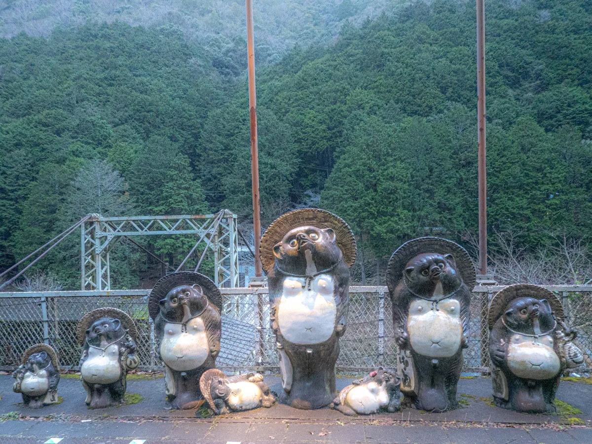 A family of large Shigaraki pottery tanuki statues beside a railing at Torokko Hozukyo Station