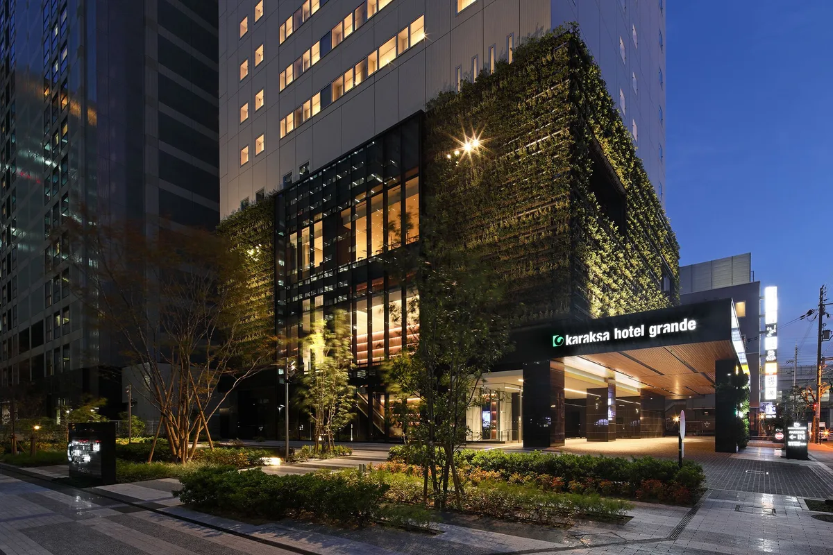 The illuminated entrance and planted facade of karaksa hotel grande Shin-Osaka Tower
