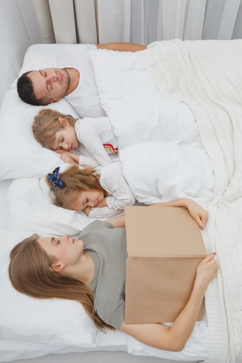 Two parents and two young children sharing one large bed