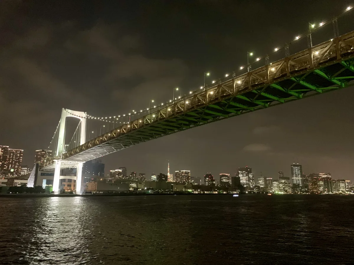 Rainbow Bridge illuminated above Tokyo Bay at night, with the Tokyo skyline beyond