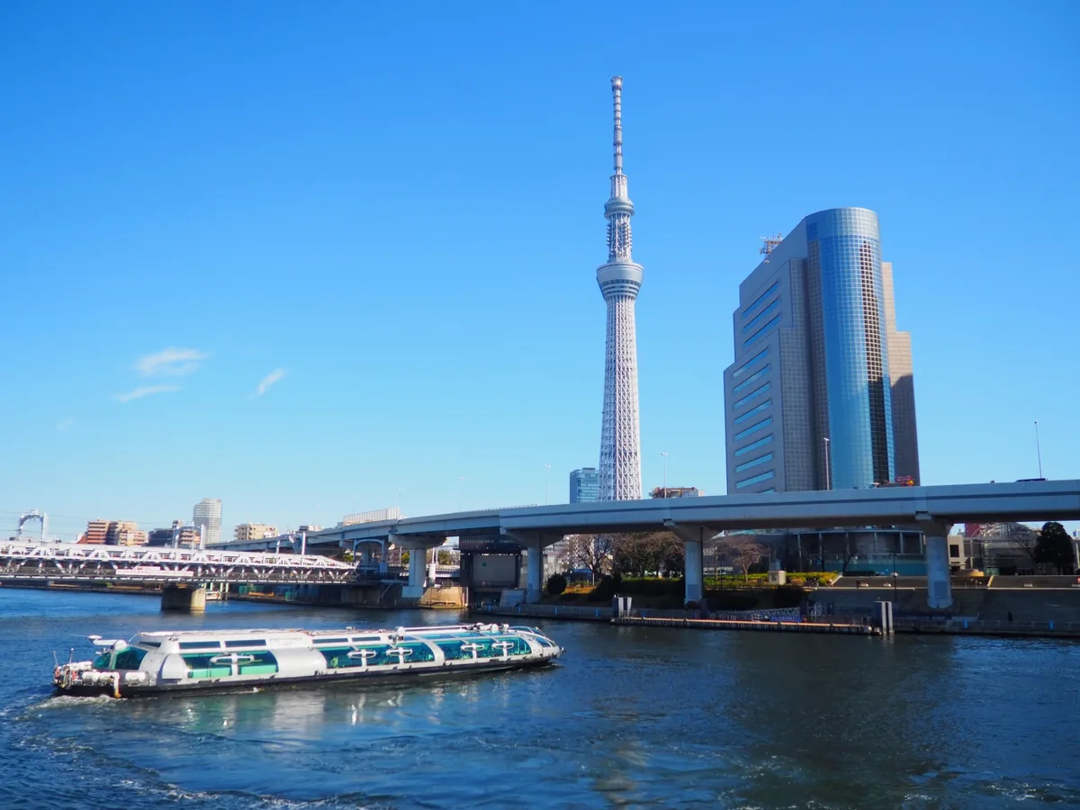 A daytime Tokyo water bus on the Sumida River with Tokyo Skytree behind it