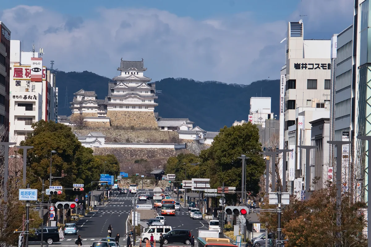 Himeji Castle seen at the end of a broad city street, with traffic and buildings in the foreground