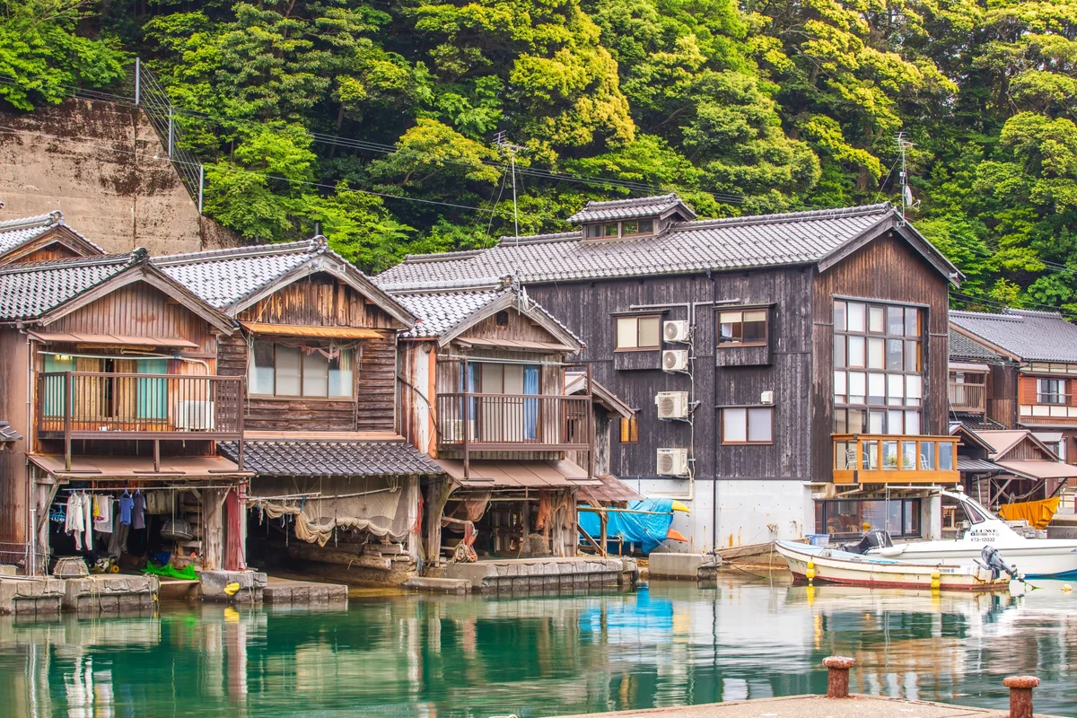 Timber boathouses and moored boats reflected in the water of Ine Bay