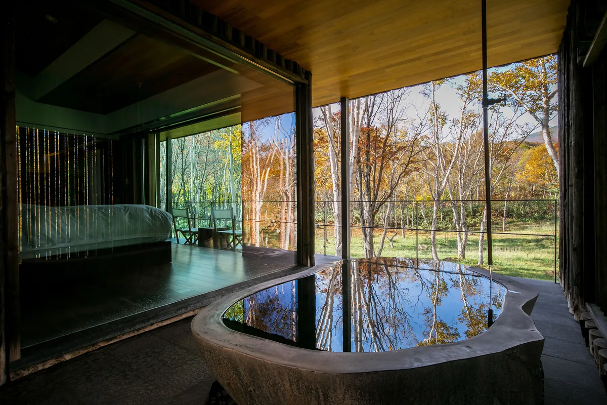 Stone open-air bath beside an indoor bathing area and autumn woodland at Zaborin