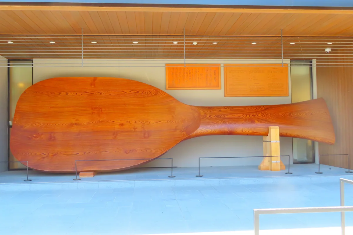 An enormous wooden shamoji rice paddle displayed horizontally behind glass in Miyajima