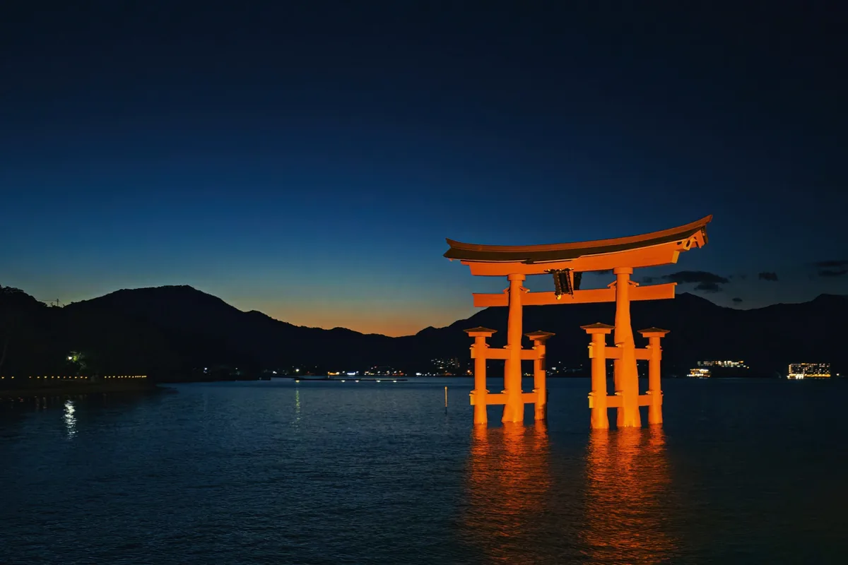 Miyajima's illuminated torii reflected in the water beneath a deep blue evening sky