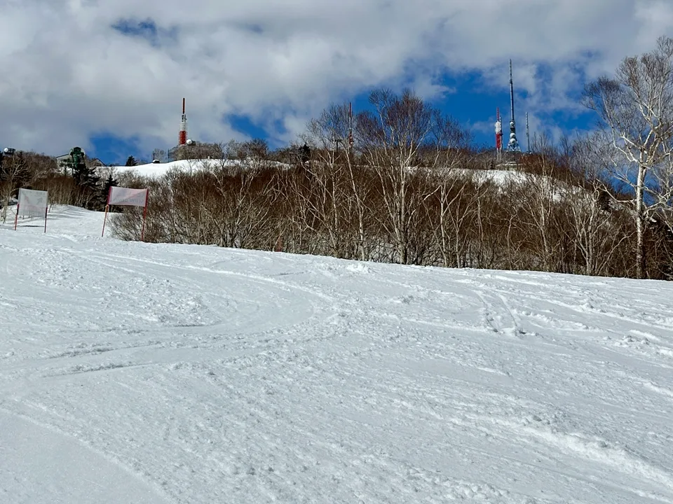 Snow-covered ski slope with trees and towers beneath a cloudy blue sky in Hokkaido