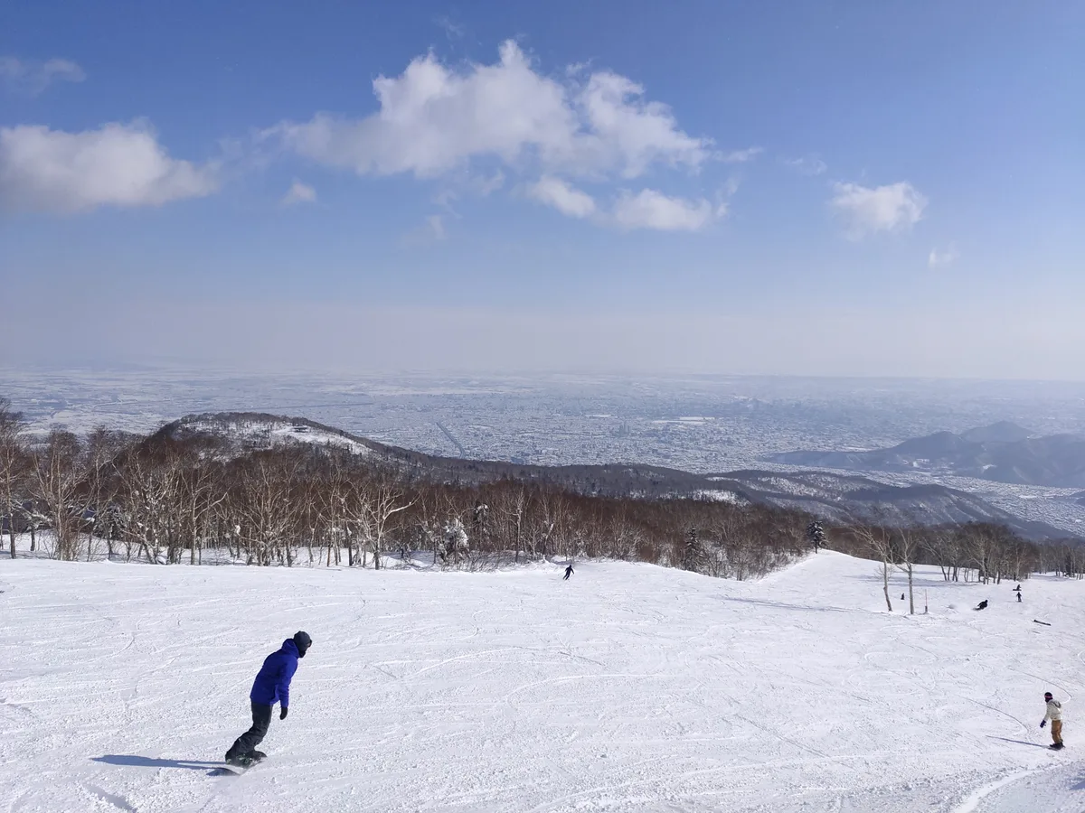 Snowboarders on a Teine Highland slope with Sapporo visible below