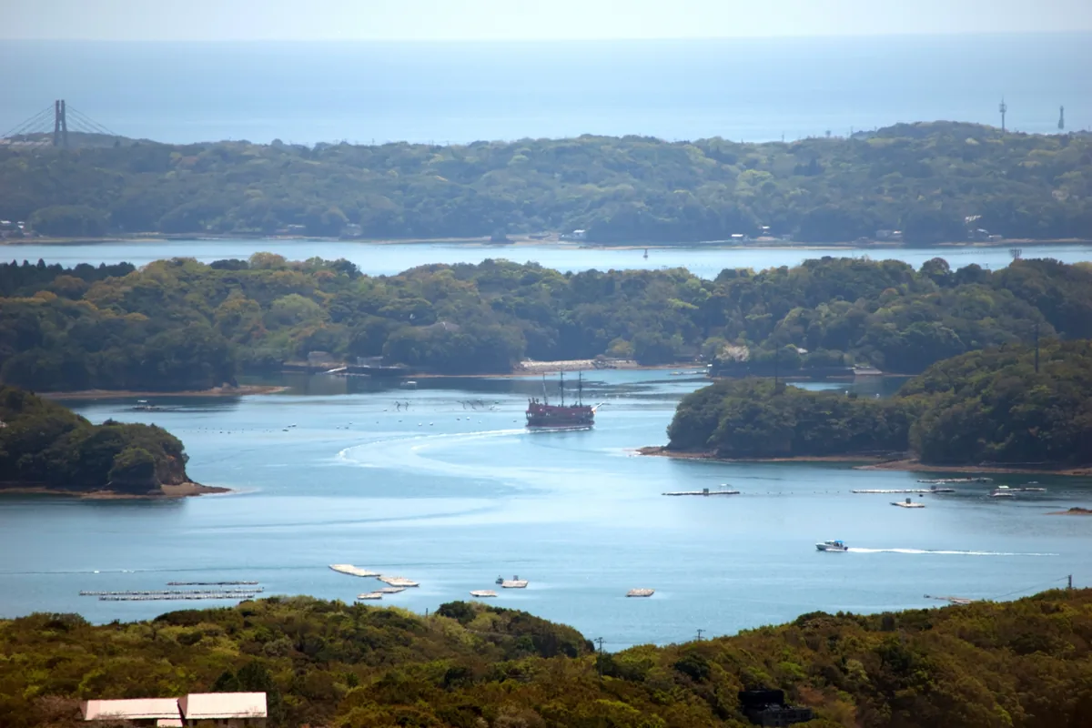 Wooded islands and boats on the blue channels of Ago Bay, viewed from a hillside