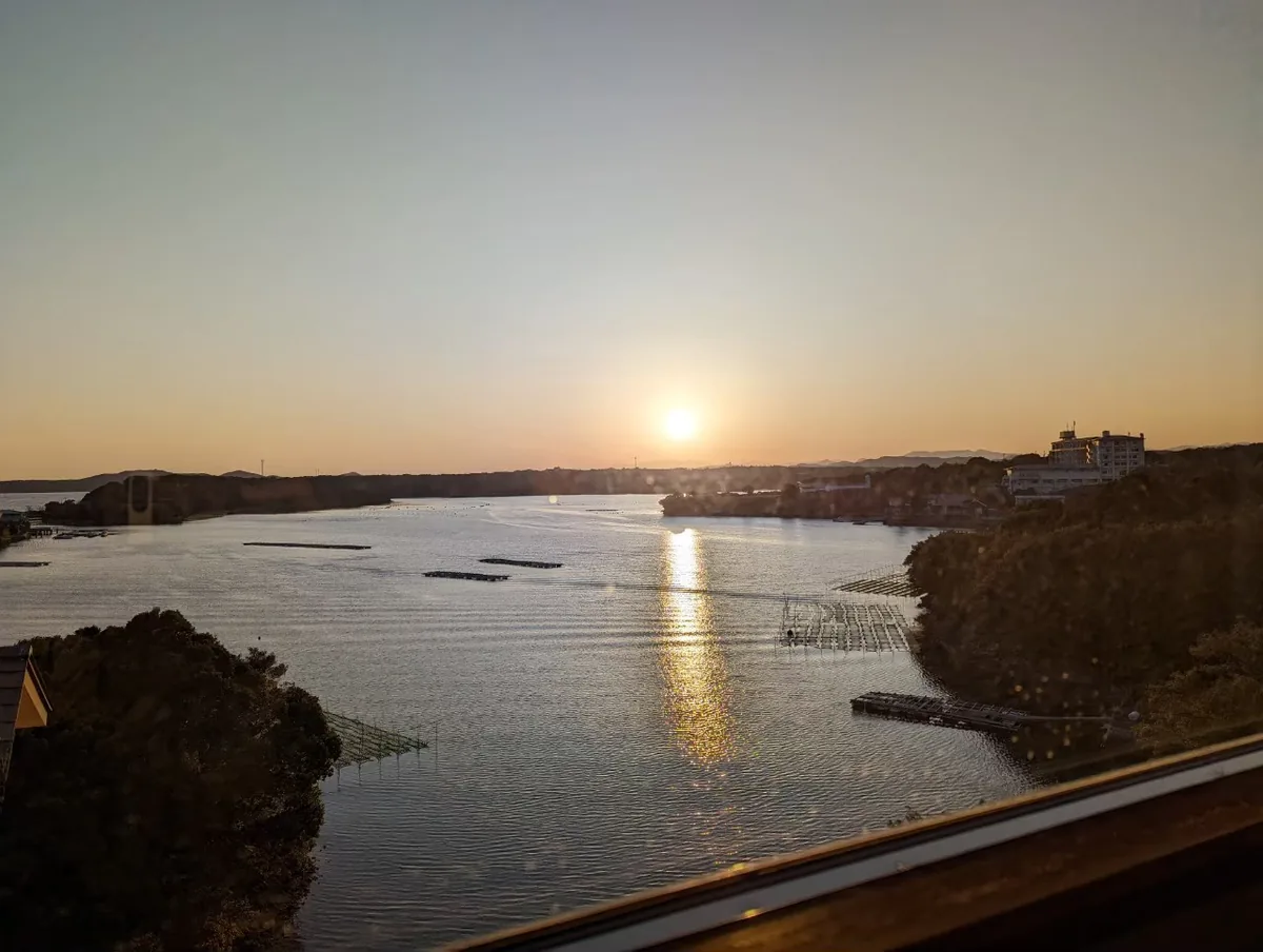 Low sunlight reflected across Ago Bay, with wooded shores and floating platforms on the water