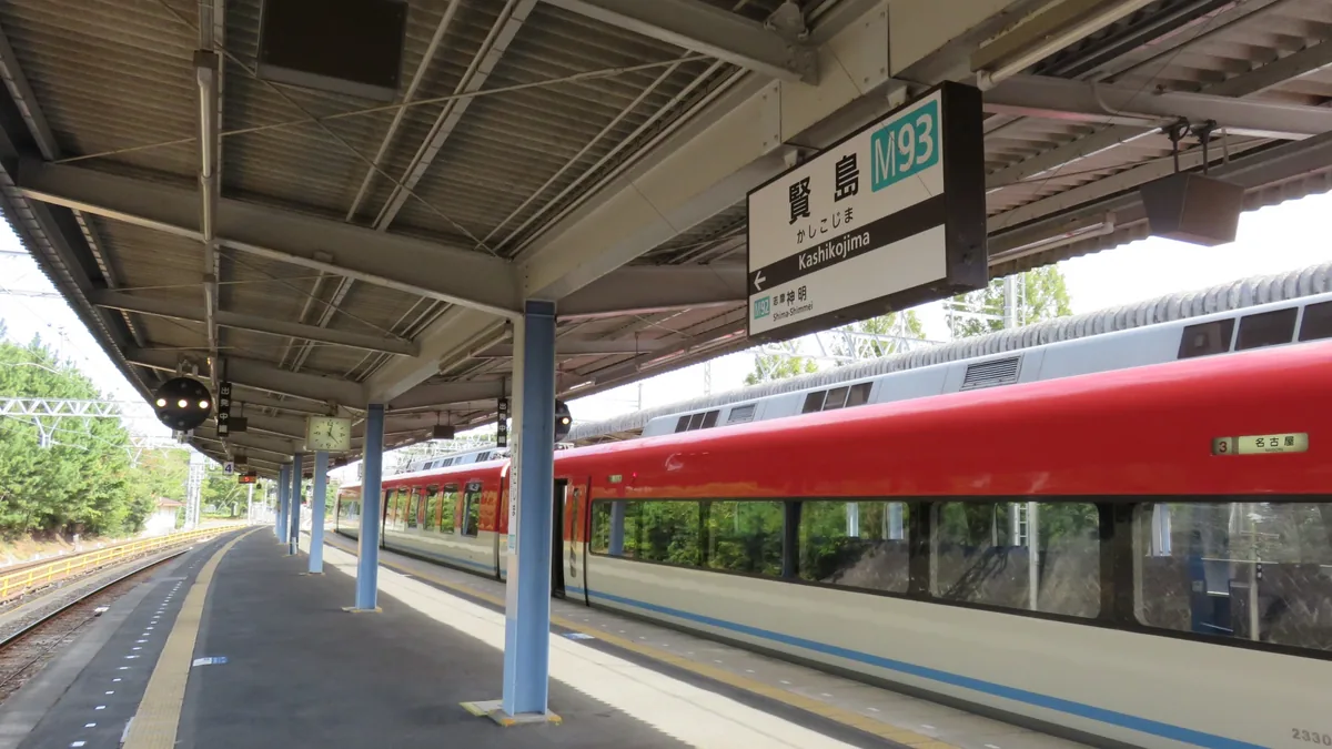 A red and white Kintetsu train beside a platform sign reading Kashikojima