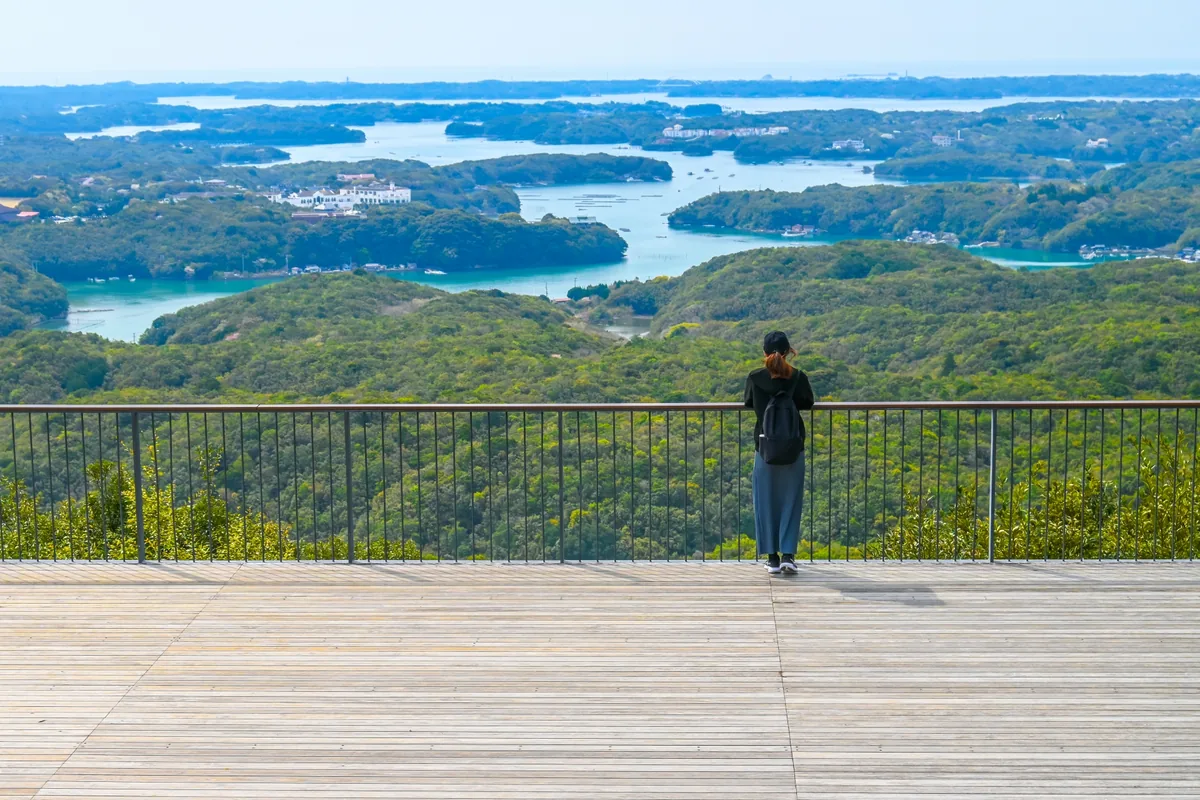 A visitor standing at the railing of Yokoyama's wooden viewing deck, overlooking Ago Bay