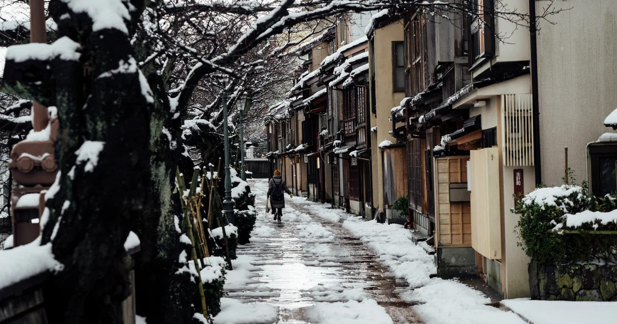 A person walking along a snowy lane beside wooden buildings in Kanazawa's Kazue-machi district