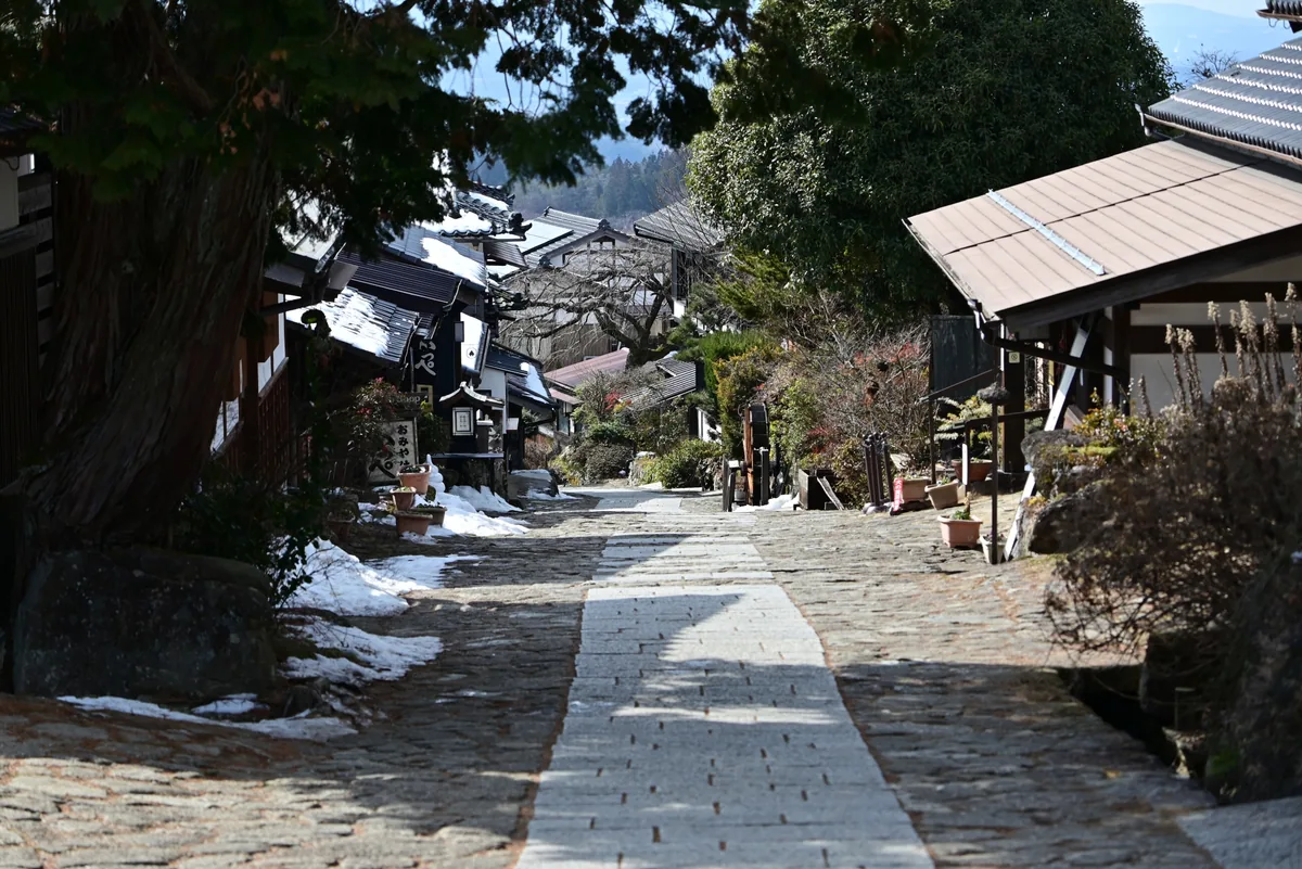 A stone-paved street with patches of snow beside buildings in Magome