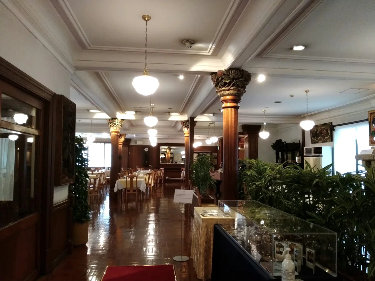 Wooden columns with carved capitals, white pendant lights and tables in the hotel dining room.