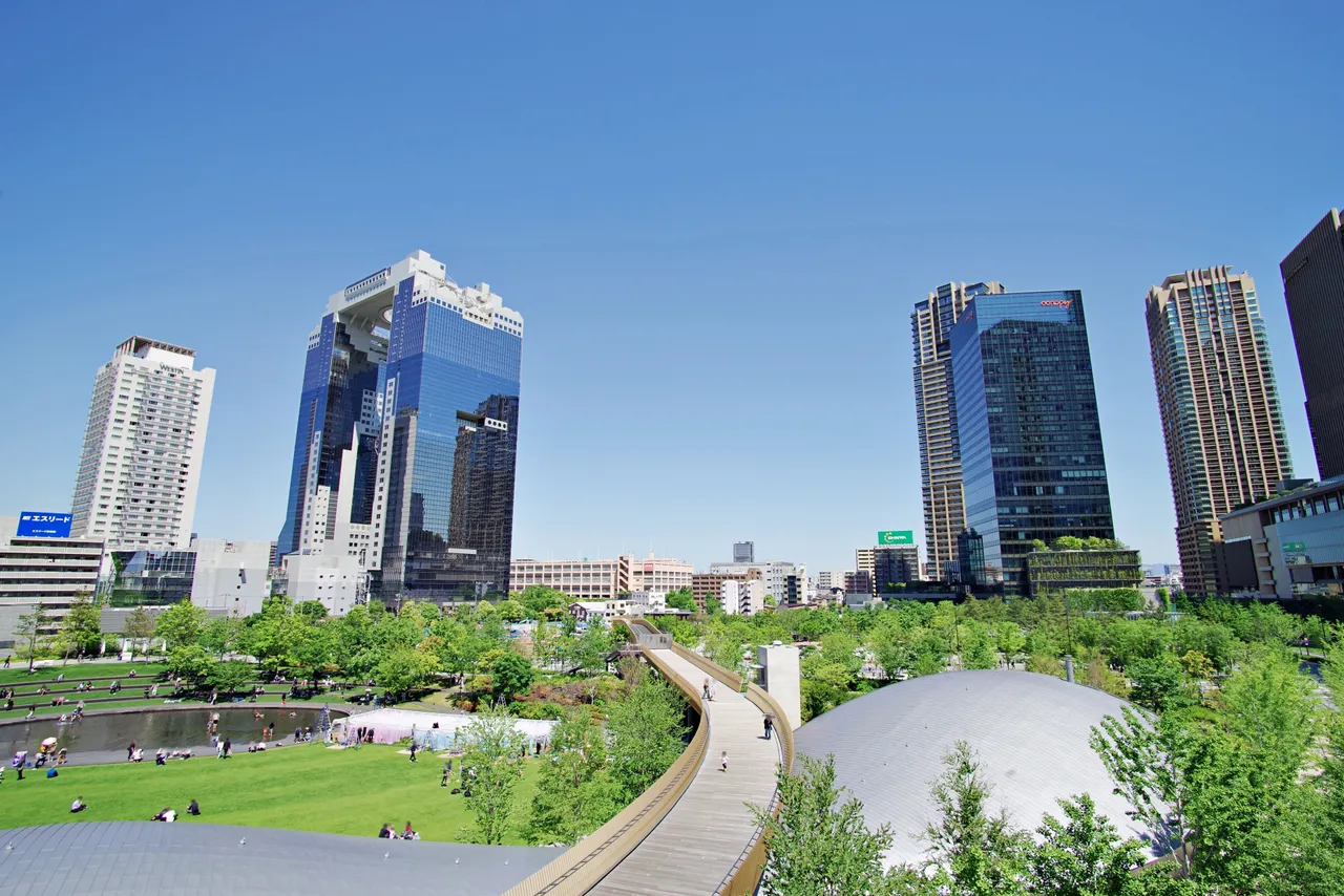 The twin towers of Umeda Sky Building beyond a green park, with other modern Osaka buildings nearby
