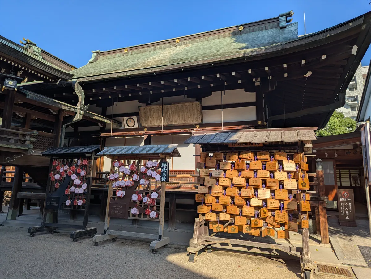 Plum-shaped and rectangular prayer plaques displayed beside a shrine building