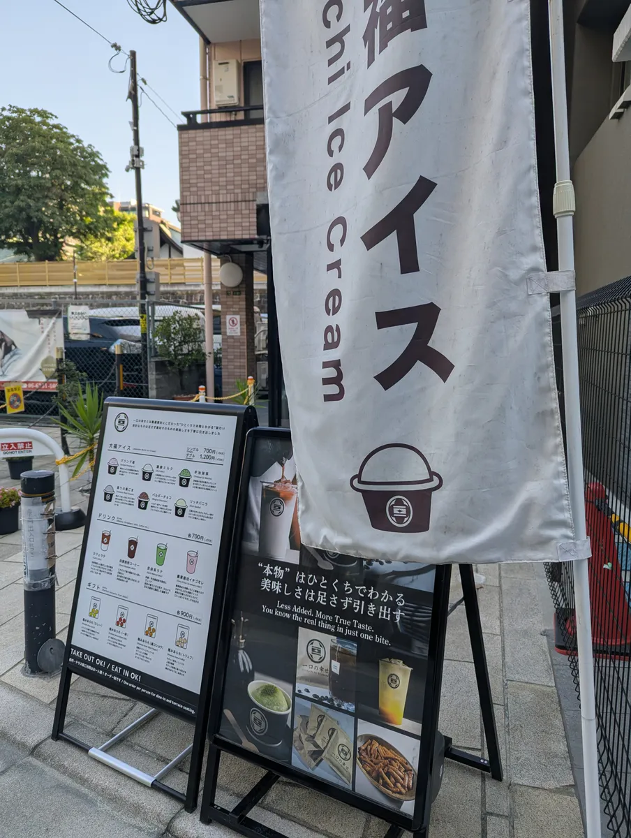 An ice cream banner and menu board outside Hitokuchi no Shiawase near Osaka Tenmangu