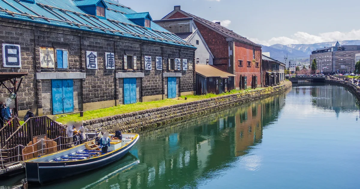A sightseeing boat on Otaru Canal beside warehouses under a blue sky