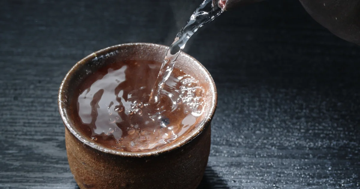 Sake being poured into a brown ceramic cup, shown as an illustrative photograph