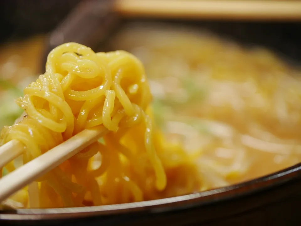 Yellow ramen noodles lifted above a bowl with chopsticks