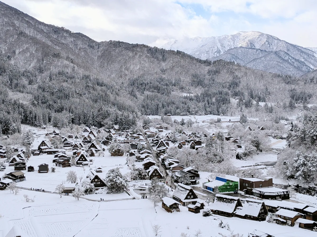 Snow-covered Shirakawa-go village and surrounding wooded mountains viewed from above