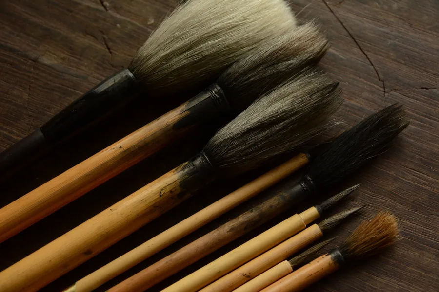 Calligraphy brushes of different sizes arranged diagonally on a dark wooden surface