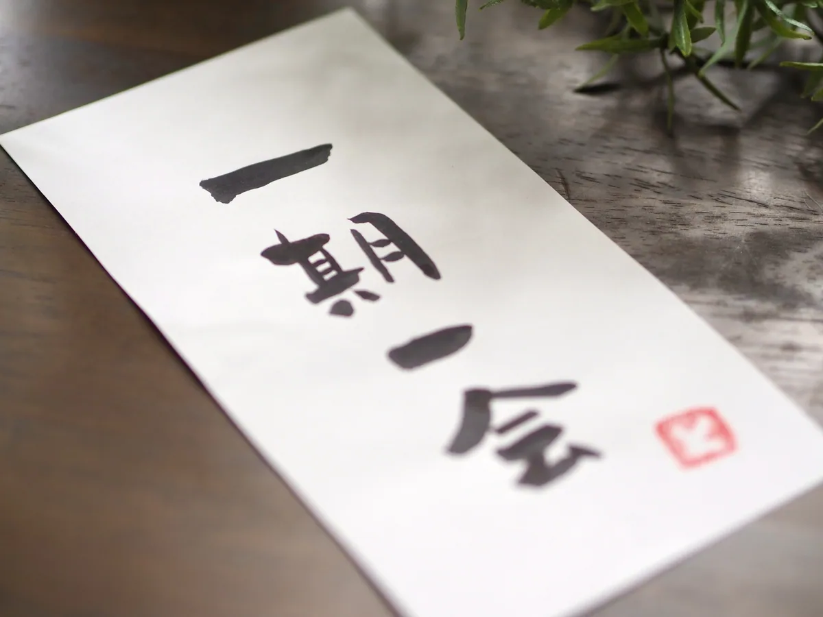 A finished sheet of calligraphy reading ichigo ichie, with a small red seal on a wooden table