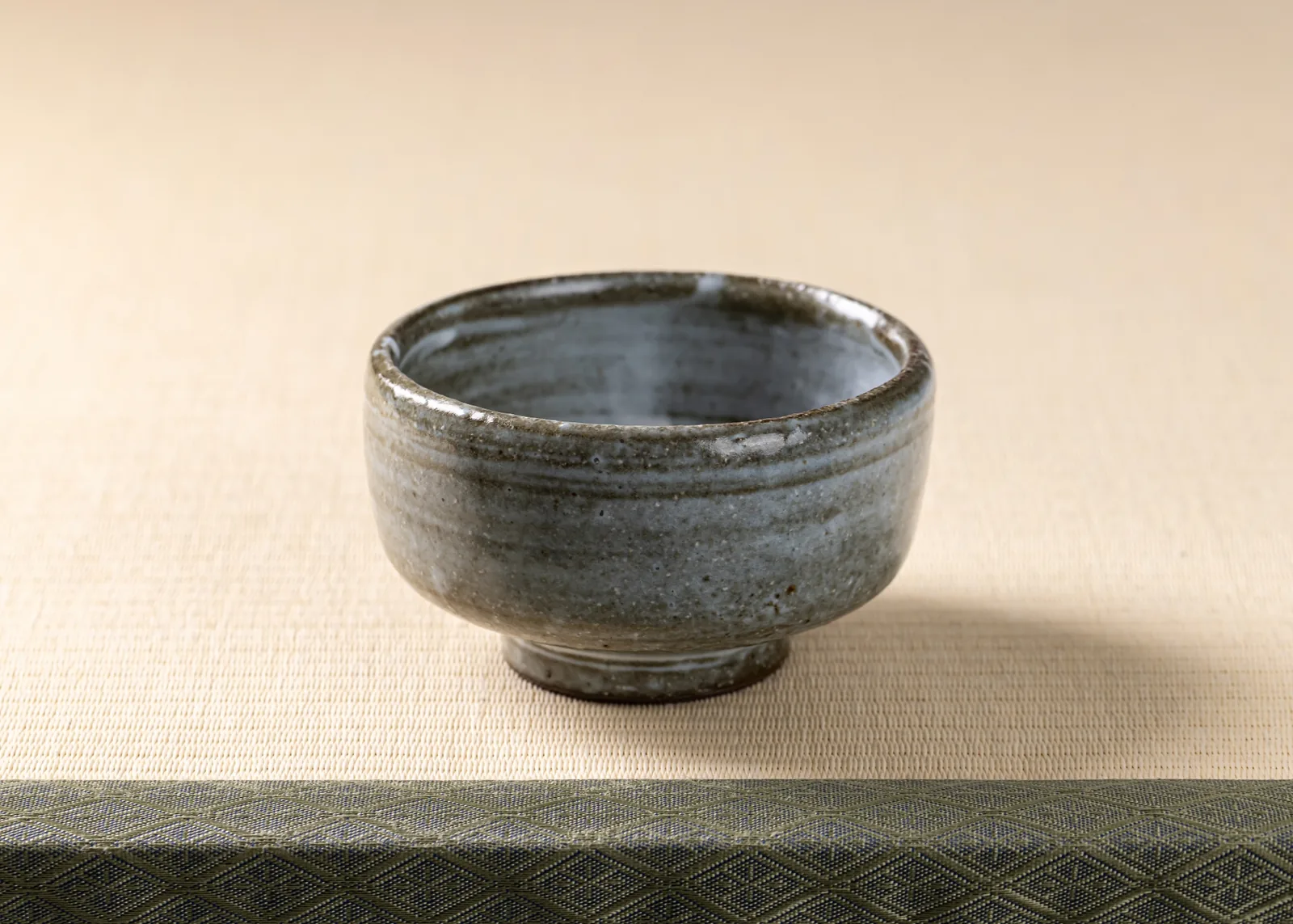 An empty, softly textured ceramic tea bowl resting on tatami