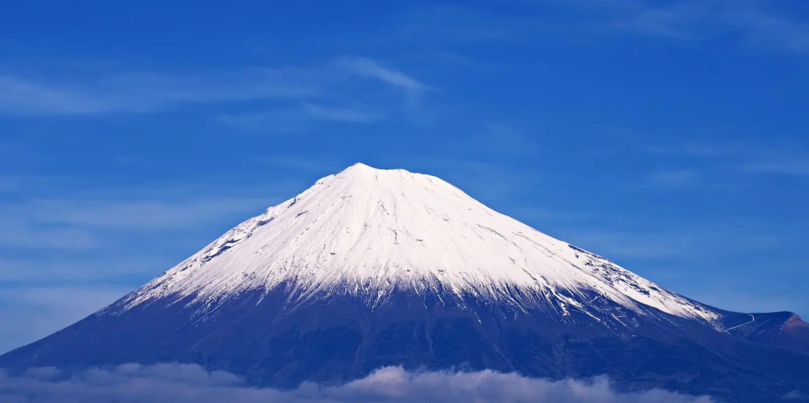 Snow traces the ridges of Mount Fuji above a band of cloud.