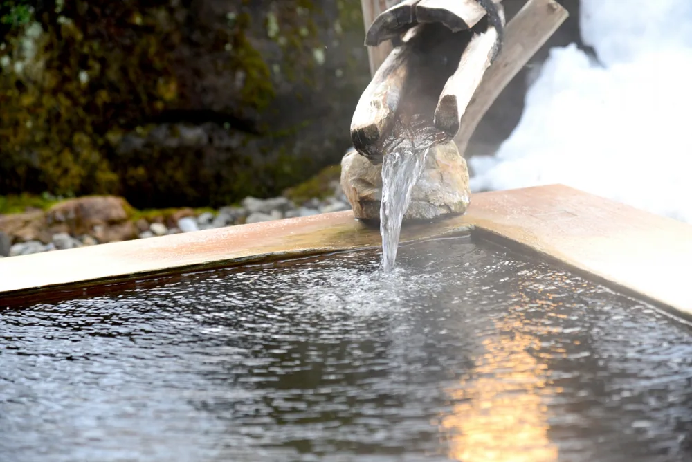 Water pouring from a rustic wooden spout into a steaming bath