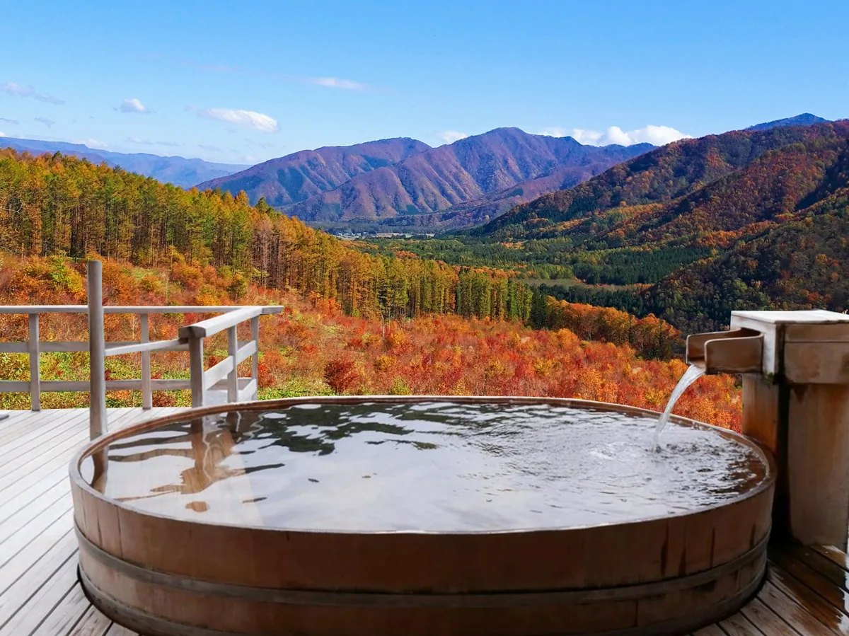 A round wooden tub on a terrace overlooking orange autumn trees and a broad mountain valley