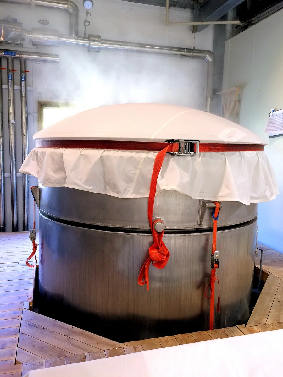 Steam rising around a covered metal vessel with a red pipe attached