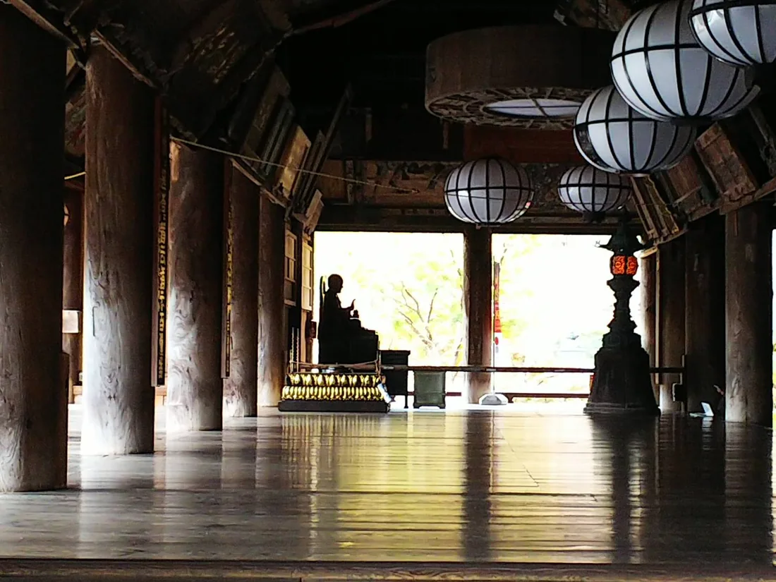 Light at the end of a dark wooden corridor, with thick pillars and a row of round hanging lanterns
