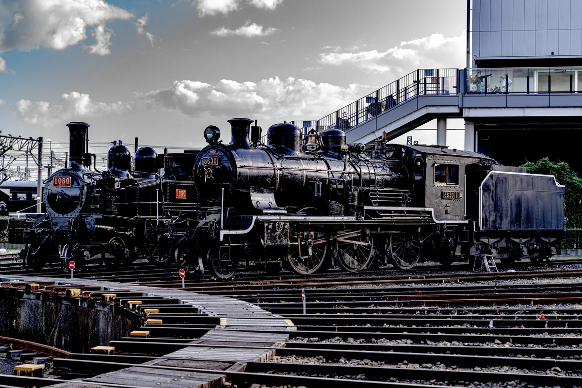 Several historic steam locomotives displayed beside railway tracks in Kyoto