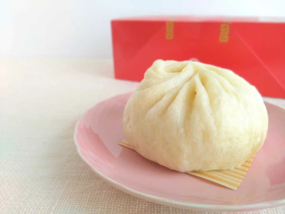 A pleated steamed pork bun on a pink plate with a red 551 HORAI box behind it