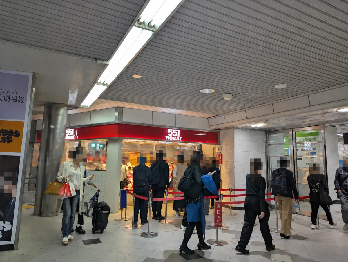 551 HORAI's red shopfront and takeaway queue at JR Osaka Station, with people's heads mosaicked for privacy