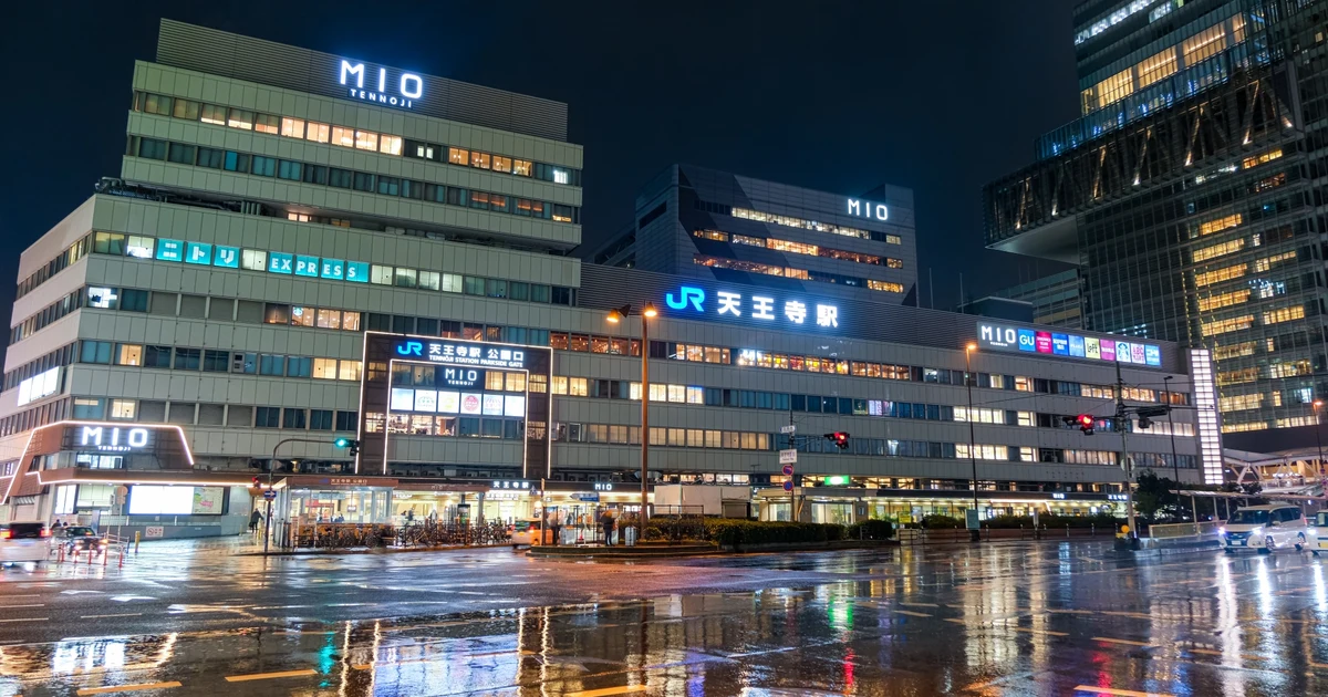Tennoji Station and MIO in Osaka at night, with station lights reflected on rain-wet pavement. Illustrative location photo, not a featured activity venue.