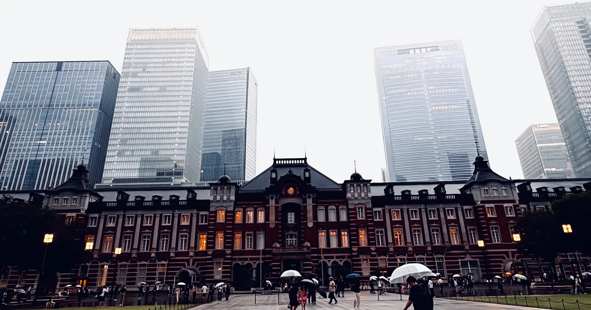 Tokyo Station and surrounding skyscrapers seen across a rain-soaked plaza