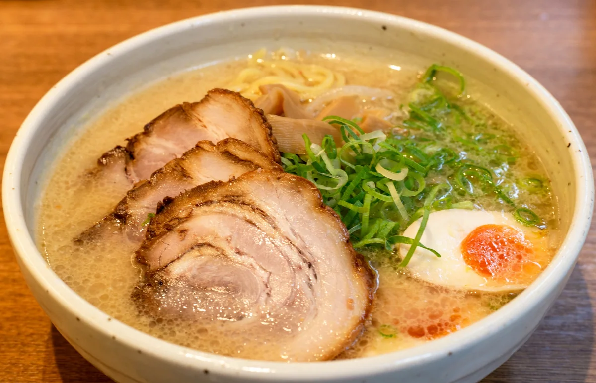 A bowl of ramen topped with sliced pork, spring onions and half an egg