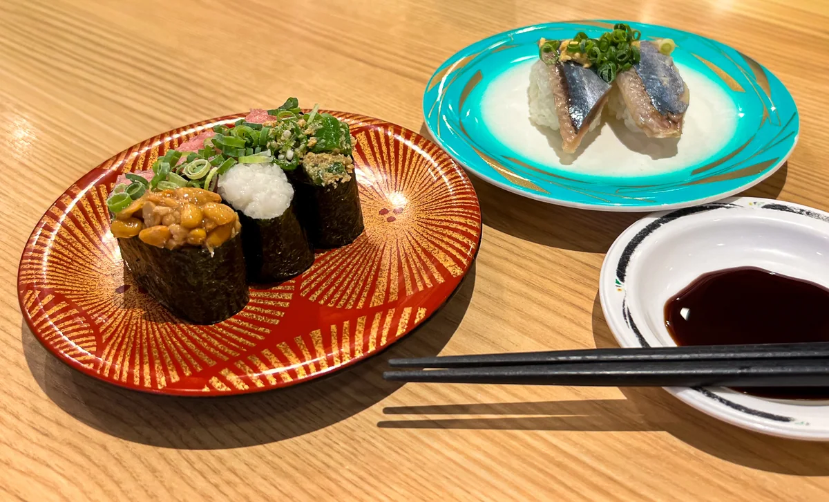 Several kinds of sushi served on individual patterned plates beside chopsticks and soy sauce