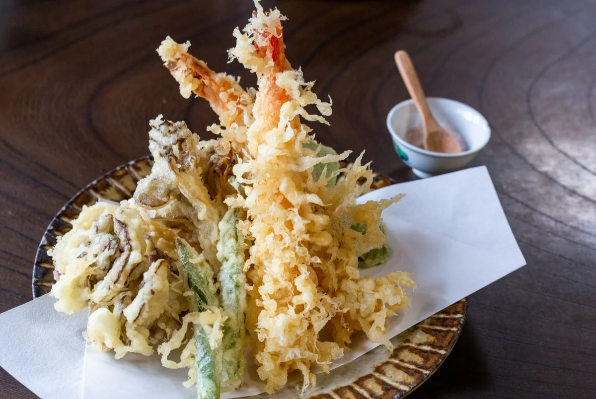 Shrimp and vegetable tempura arranged on paper in a woven serving basket