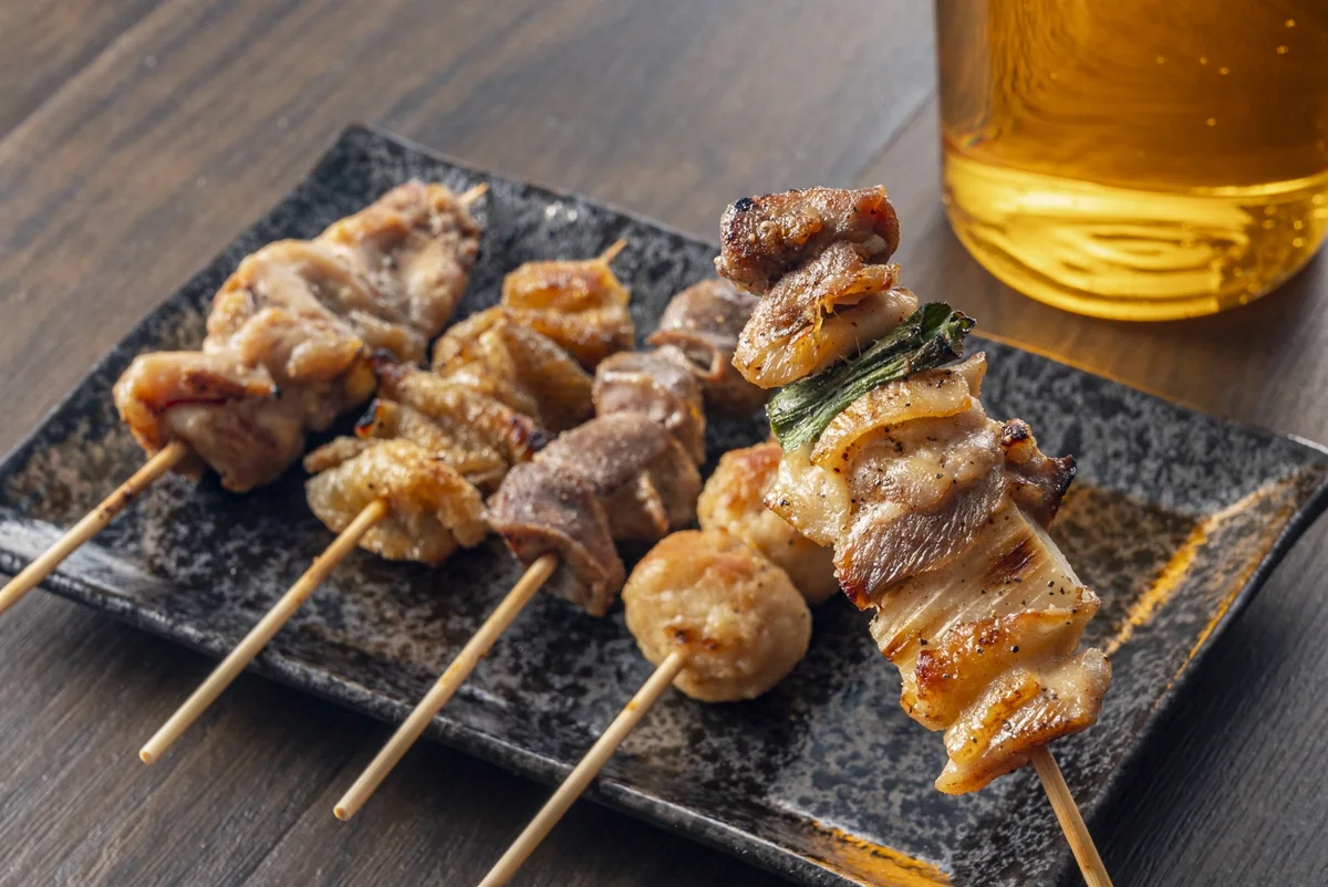 Grilled skewers arranged on a dark plate, including chicken with leek