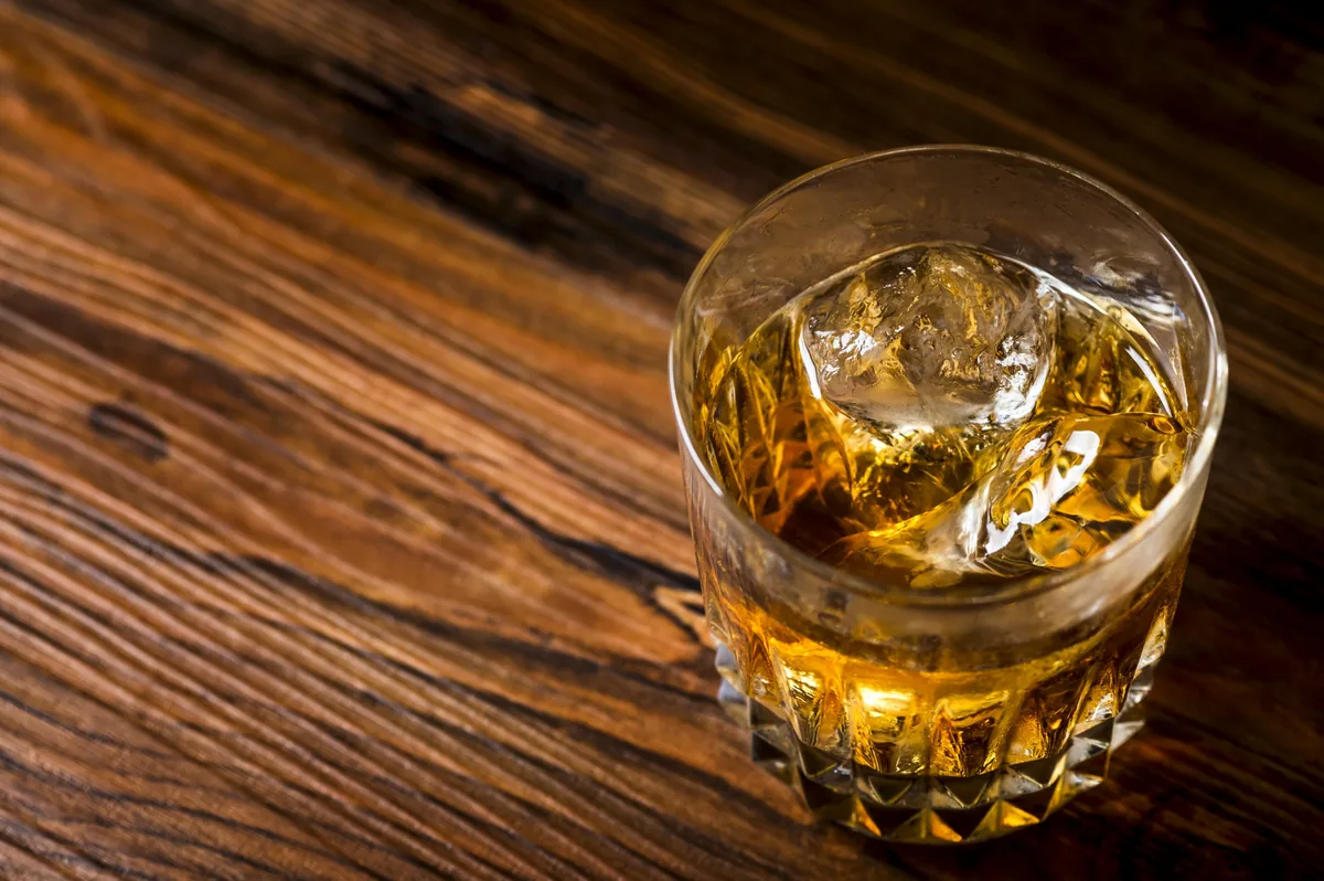 A glass of amber whisky with ice on a wooden table