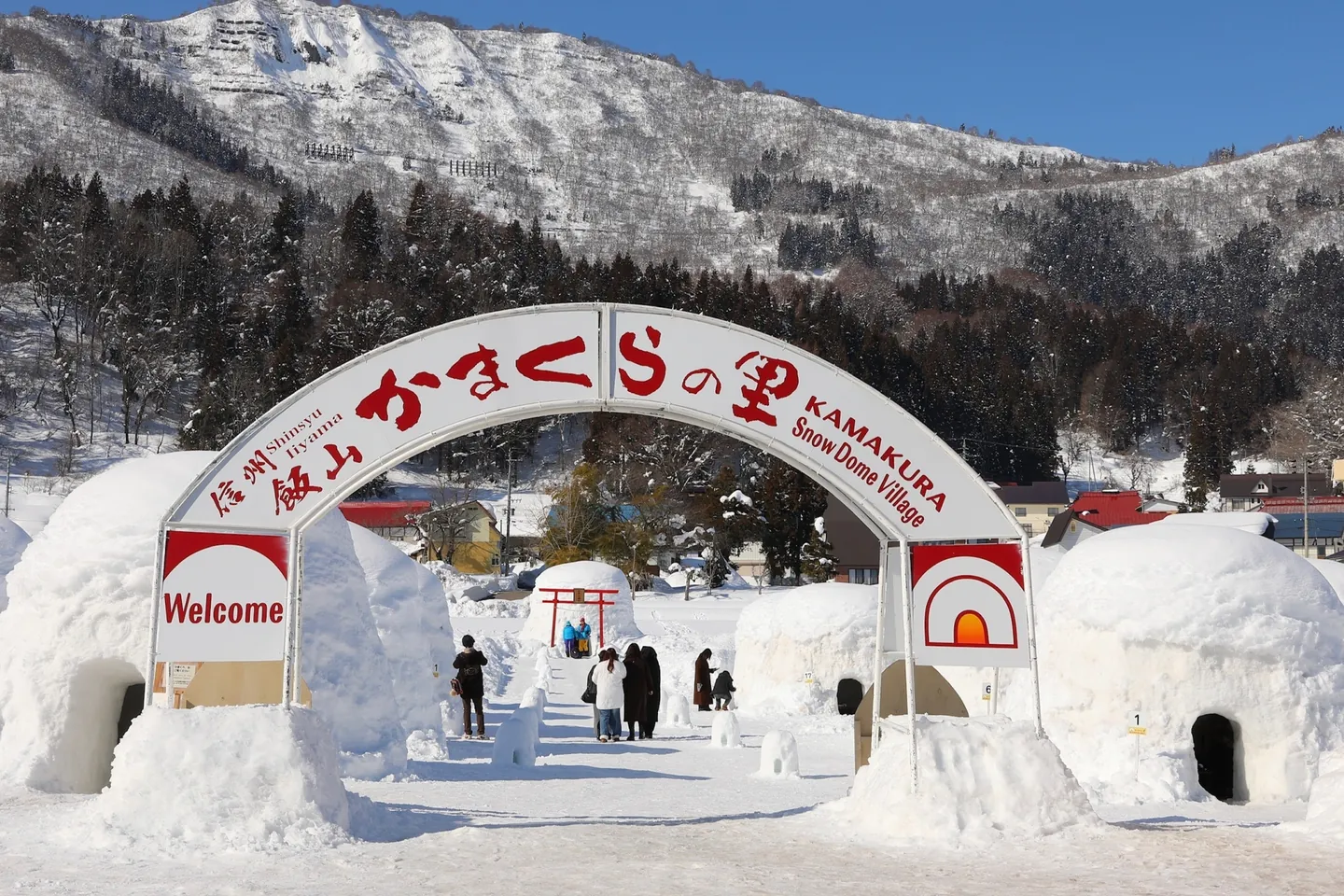 Visitors entering Iiyama's Kamakura Snow Dome Village through an arch beside large snow huts