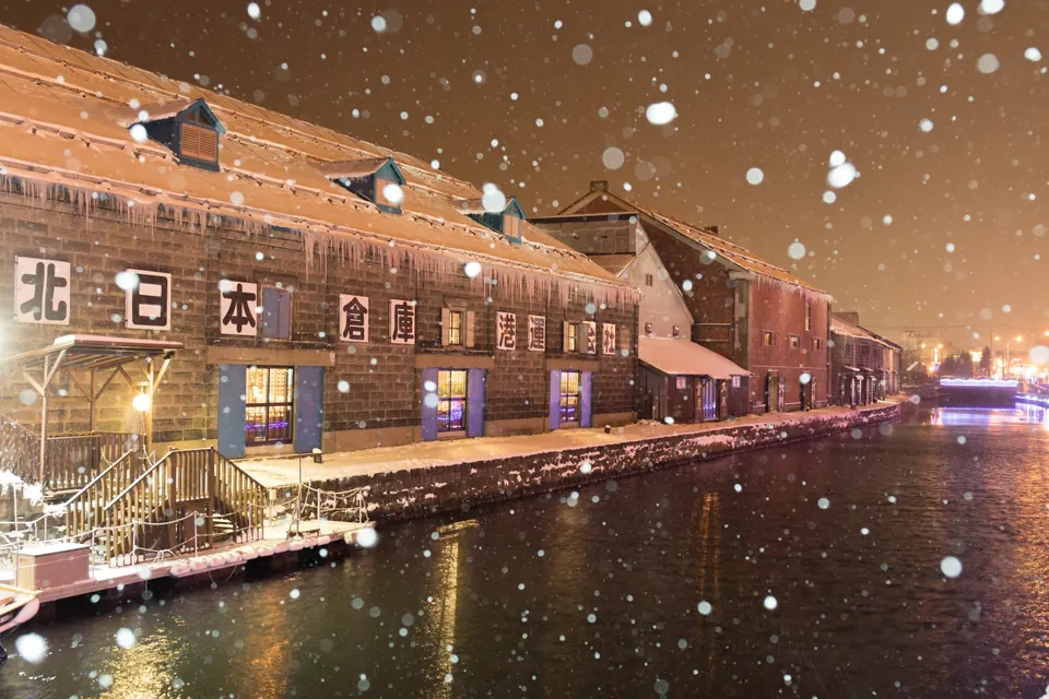 Snowflakes falling over Otaru Canal beside illuminated warehouse buildings